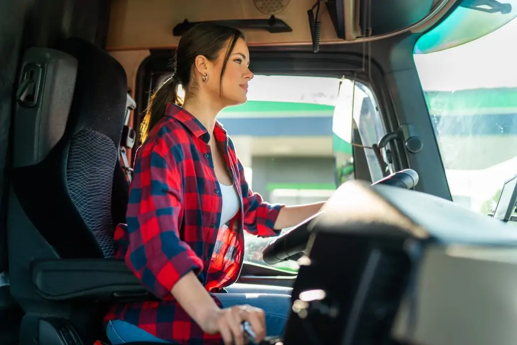 young woman professional truck driver sitting and driving big truck cross country.